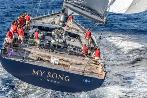 Equipaggio in rosso sul My Song yacht, che solca le onde blu. La vela nera e bianca cattura il vento.