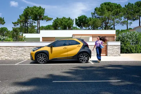 Une jeune femme se dirige vers sa voiture jaune et noire, une **voiture jeune permis automatique** parfaite pour débuter.