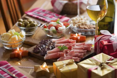 Pyszne menu na sylwestra w domu: deska wędlin i serów, oliwki, pomidorki z mozzarellą, orzechy, wino i prezenty.