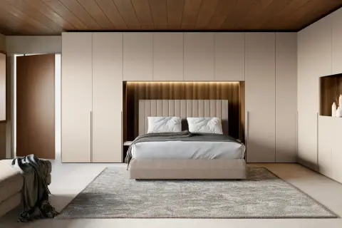 Una moderna zona notte all'ingresso, con letto centrale, armadi a muro e un pouf.