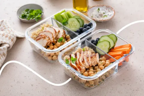 Zwei Behälter für Meal Prep mit Hähnchenbrust, Kichererbsen, Quinoa, Gurke, Karotten und Blaubeeren.