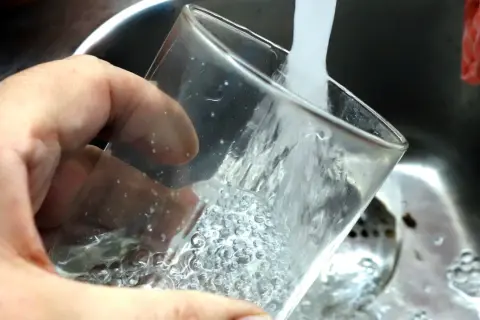 En hand håller ett glas som fylls med vatten från en kran. Ja, kan man drikke vann fra springen i Sverige, det är rent och gott!
