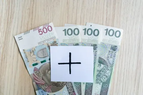 Polskie banknoty 500 i 100 zł. Na białej kartce symbol plusa, sugerujący dodatkowe środki, np. specjalny zasiłek opiekuńczy.