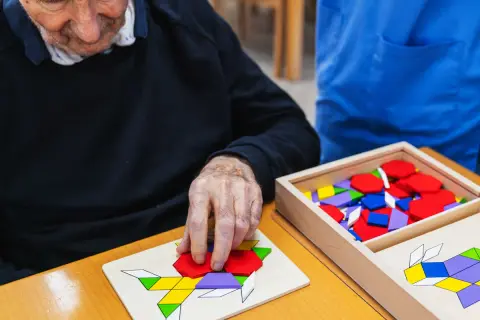 Un senior concentré assemble un puzzle coloré, un jeu mémoire senior stimulant.