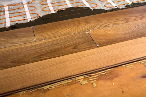 Close-up of plank flooring installation over underfloor heating. Wooden planks are being laid with spacers, showing the adhesive and heating elements beneath.