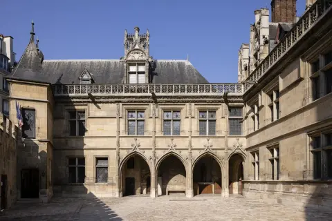Hof des Musée de Cluny mit gotischer Architektur, Spitzbögen und filigranen Verzierungen unter blauem Himmel.