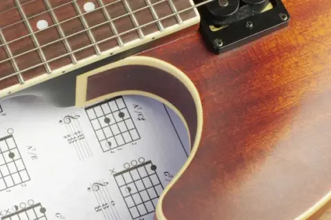 Gitarrenhals über Notenblättern mit Akkorddiagrammen. Perfekt für Gitarre Grundlagen.