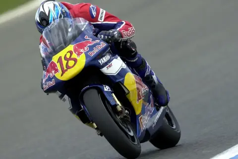 Piloto con casco azul y rojo, traje de carreras Red Bull y moto Yamaha número 18, en plena curva. Jean Michel Bayle en acción.