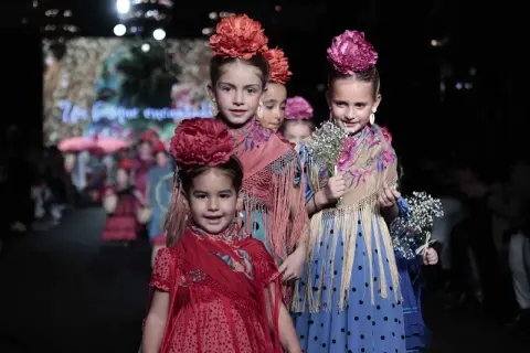 Niñas desfilan con trajes de flamenca, mostrando cómo vestir a un niño de flamenco con flores y mantones.