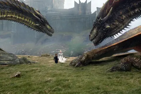 Zwei Drachen blicken sich gegenüber, während Daenerys und Tyrion im Gras stehen. Die epische **Titelmusik Game of Thrones** beginnt.