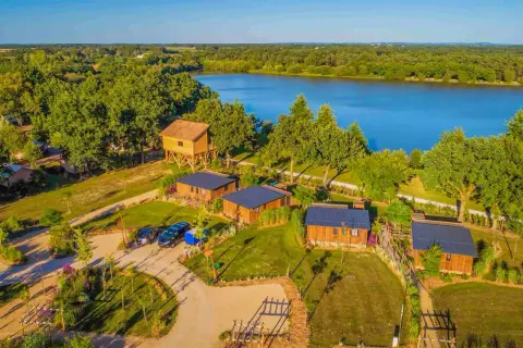Vue aérienne de chalets en bois et d'une cabane perchée près du lac de la Chausselière, entourés de verdure luxuriante.