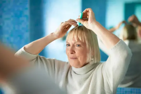 Kobieta stosuje preparat na skórę głowy, by zaradzić problemowi, jakim jest menopauza a wypadanie włosów.