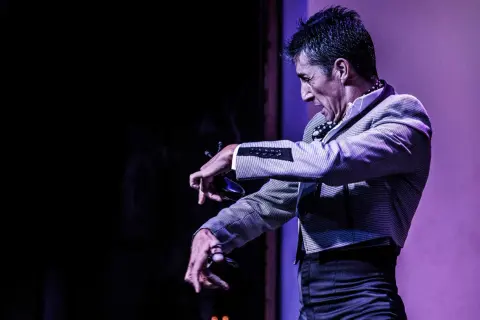 Un hombre con traje a cuadros realiza un apasionado flamenco baile, con las manos extendidas y castañuelas.