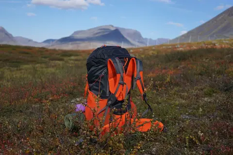 En stor ryggsäck står redo för mat utomhus i fjällterräng. En liggunderlag och en lila kudde syns vid sidan.