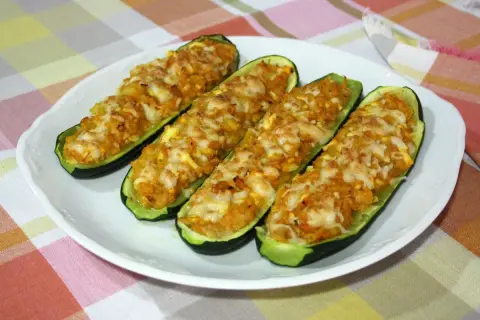 Cuatro calabacines rellenos, gratinados con queso, servidos en un plato blanco sobre un mantel a cuadros.