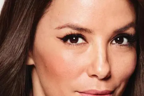 Primer plano de una mujer con pelo fosco y oscuro, ojos marrones con delineado cat eye y piel con rubor.