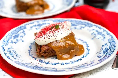 En bit saftig sockerkaka med pepparkakskrydda, toppad med vispad grädde och strössel. Serveras på en vacker blåvit tallrik.