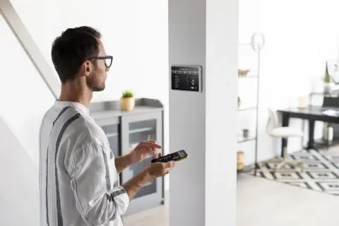 Un homme utilise une télécommande pour installer une alarme sur un écran tactile mural.