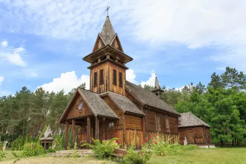 Drewniany kościółek z wieżą i krzyżem, otoczony lasem. Piękny przykład kościołów w Polsce.
