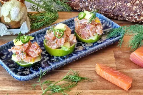 Delicioso tartar de salmón y aguacate servido en mitades de lima, decorado con jalapeño y eneldo.