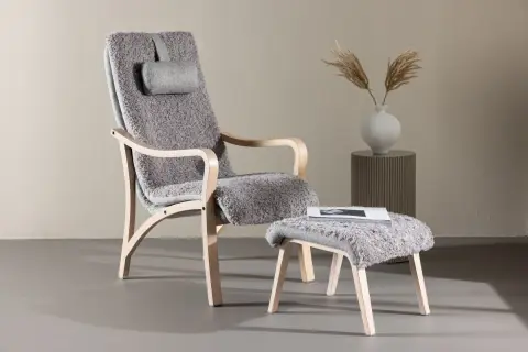 En bekväm trä fåtölj med grå fårskinnsklädsel och en matchande pall. Perfekt för en mysig läshörna.