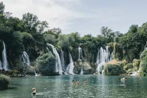 Atemberaubende Wasserfälle in Bosnien, Natur pur. Menschen genießen das kühle Wasser in einem türkisfarbenen See, umgeben von üppiger Vegetation.