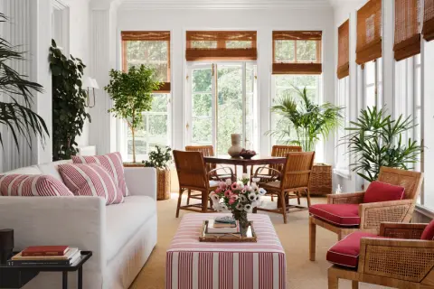 Bright sunroom with white sofa, striped ottoman, rattan chairs, and lush plants. Inspiring sunroom decorating ideas for a fresh, airy feel.