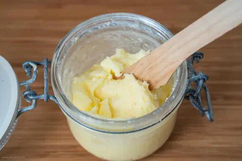 Frisch gemachtes, gelbes Butter in einem Glas mit einem Holzspatel. So einfach kann Butter selber machen sein!