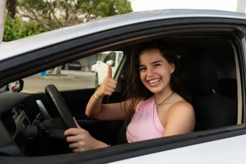 Joven sonriente en coche, pulgar arriba. ¡Ya sabe hasta que edad se puede conducir en España!