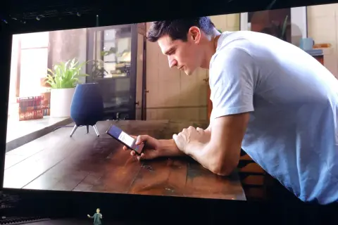 Un homme utilise son téléphone pour contrôler son **galaxy home**. Un haut-parleur intelligent est visible sur la table.