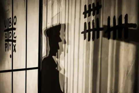 Shadows cast by bars and a figure on a wall with tally marks and letters. This image illustrates how to avoid shadows in indoor photography by using them creatively.