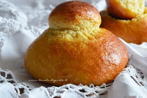 Brioches siciliane ricetta originale con strutto, dorate e soffici, su un pizzo bianco.