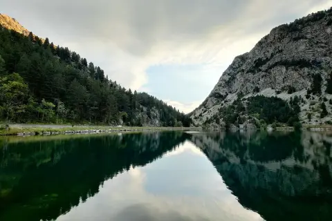 Reflejos perfectos en el ibon de Baños, rodeado de bosques y montañas rocosas. Un paisaje sereno y majestuoso.