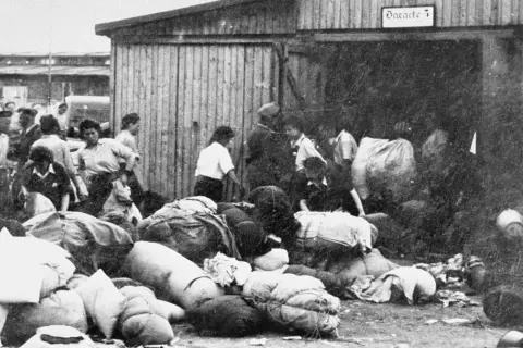 Ludzie z bagażami przed barakiem w Auschwitz. To krótkie streszczenie tego, co działo się w obozie.