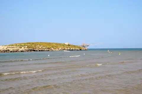 La chianca di Vieste, con la sua struttura in legno sul mare, si staglia contro il cielo azzurro. L'acqua cristallina invita a un bagno rinfrescante.
