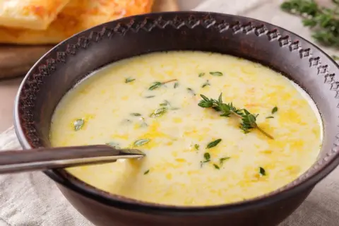 A creamy zupa na rosole, garnished with fresh thyme, served in a rustic bowl with a spoon. In the background, golden-brown toasted bread.