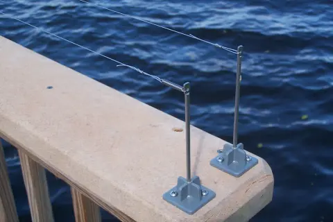 Deux piquets de pêche sur un garde-corps en bois, prêts à attraper un poisson. L'eau bleue ondule derrière.