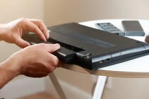 Dłonie wyjmują baterię z laptopa. To pierwszy krok, by sprawdzić stan baterii w laptopie i zadbać o jego wydajność.