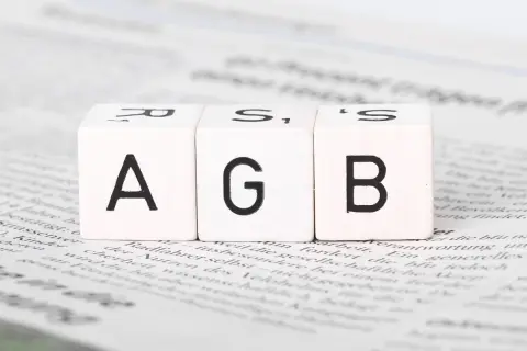 Drei Würfel mit den Buchstaben A, G, B liegen auf Zeitungstext. Ein wichtiger Schritt, um AGB zu erstellen.