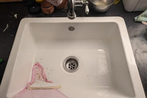 Un évier blanc avec un robinet chromé. Un outil blanc est utilisé pour aider à comment enlever un évier collé au silicone.