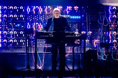 Hans Zimmer w Krakowie, na tle świecącej ściany syntezatorów i kabli, tworzy magiczną atmosferę.