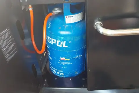Niebieska butla z gazem marki GASPOL, podłączona wężem do grilla. To odpowiednia butla do grilla gazowego, zapewniająca zasilanie.
