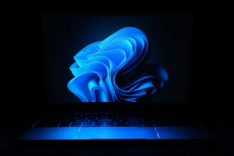 Laptop z niebieskim podświetleniem klawiatury i ekranem z abstrakcyjnym motywem. Dowiedz się, jak ustawić hasło na laptopa, by chronić swoje dane.