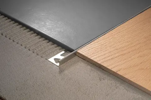 Détail d'un raccord de sol entre carrelage gris et parquet bois, avec une plinthe métallique.