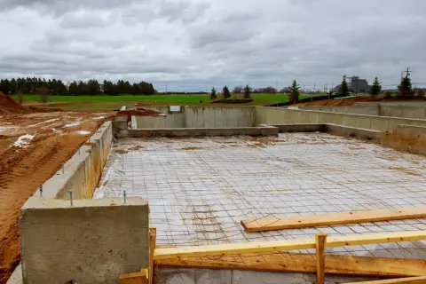Fundament betonowy w budowie, z widocznymi zbrojeniem i folią. Trudno oszacować ile bloczków betonowych na fundament zużyto.