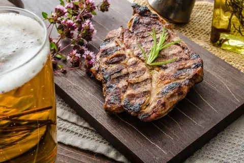 Succulenta grigliata con rosmarino, accompagnata da una birra dorata e fiori di origano.