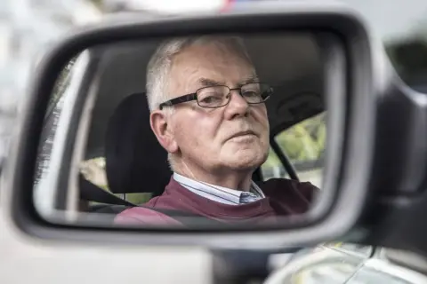 Älterer Mann mit Brille im Rückspiegel, der sich fragt, warum das Auto quietscht.