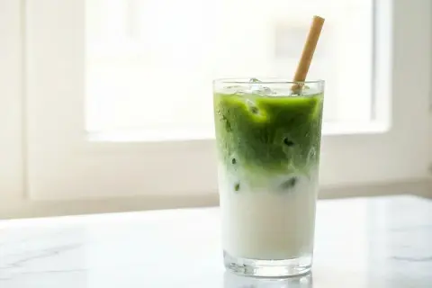 Un cocktail matcha glacé, avec du lait et une paille en bambou, sur un fond lumineux.