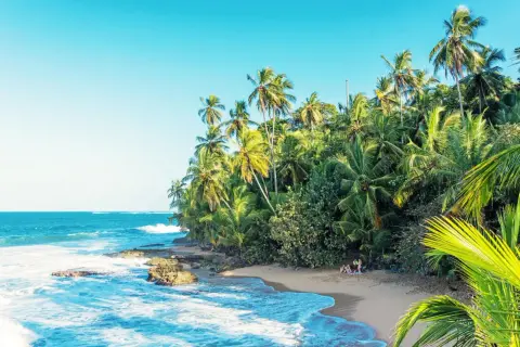 En tropisk strand i Costa Rica med vajande palmer, turkost hav och en liten grupp människor som njuter av solen.