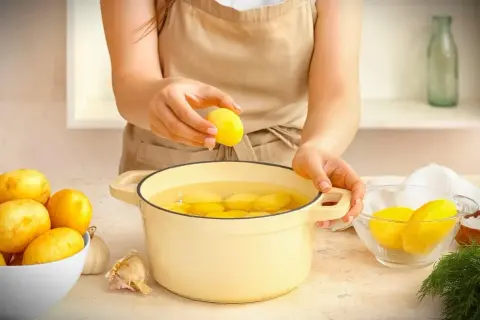 Hände legen Kartoffeln in einen Topf mit Wasser. Die Kochzeit für Kartoffeln beginnt jetzt.